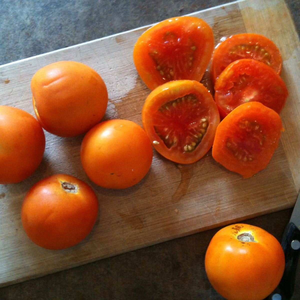 Petite Tomate Jaune Flammée sur une planche à découper à côté d&#39;un couteau, Tourne-Sol.