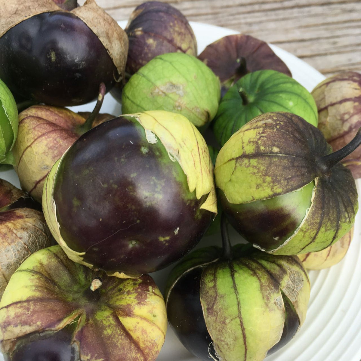 Une assiette de fruits sur une surface en bois avec des salsas Tourne-Sol Tomatillo Mauve.