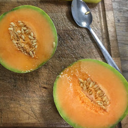 Un Melon Oka mûr à la croûte verte, coupé en deux sur une planche à découper Tourne-Sol.